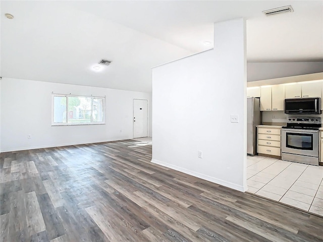 kitchen with cream cabinets, light hardwood / wood-style floors, lofted ceiling, and appliances with stainless steel finishes