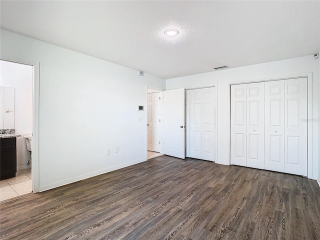 unfurnished bedroom featuring ensuite bathroom, dark hardwood / wood-style flooring, and two closets