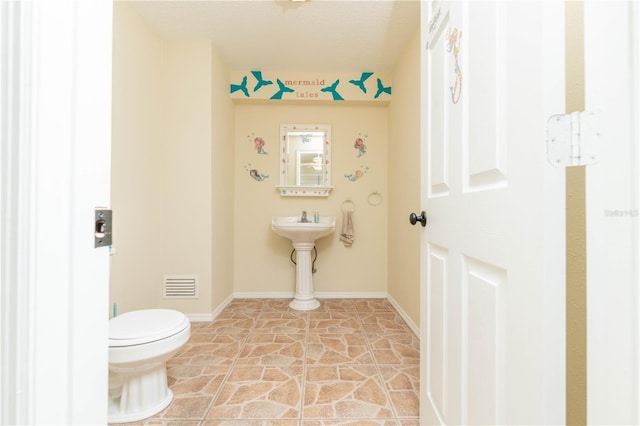 half bath with toilet, stone finish flooring, visible vents, and baseboards