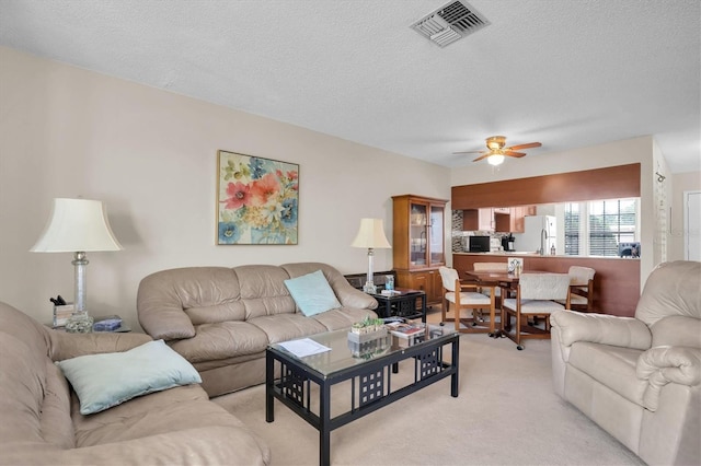 living room with a textured ceiling, light colored carpet, and ceiling fan