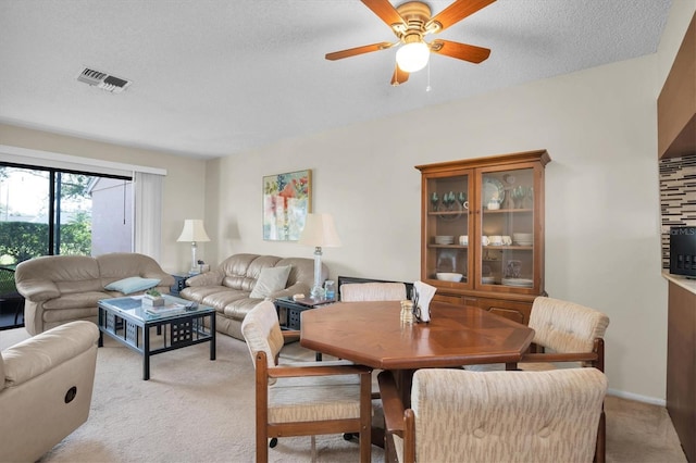 dining area featuring ceiling fan, light colored carpet, and a textured ceiling