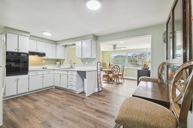 kitchen with black oven, light wood-type flooring, sink, and white cabinets