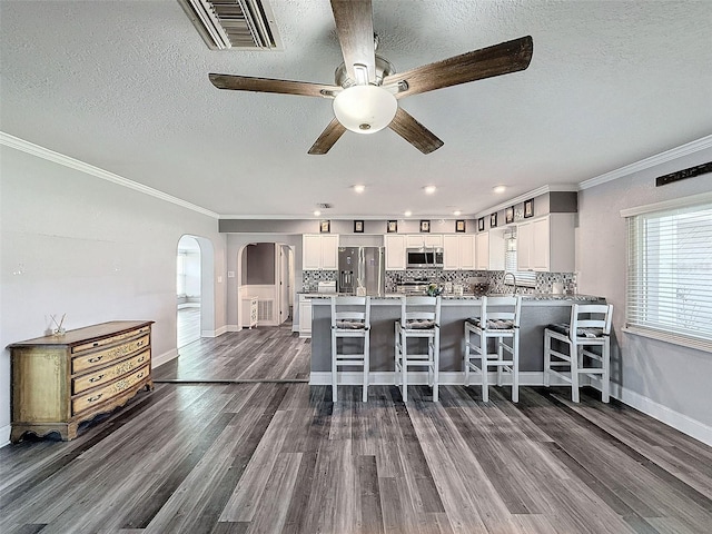 kitchen featuring dark wood-type flooring, white cabinets, a kitchen breakfast bar, crown molding, and appliances with stainless steel finishes