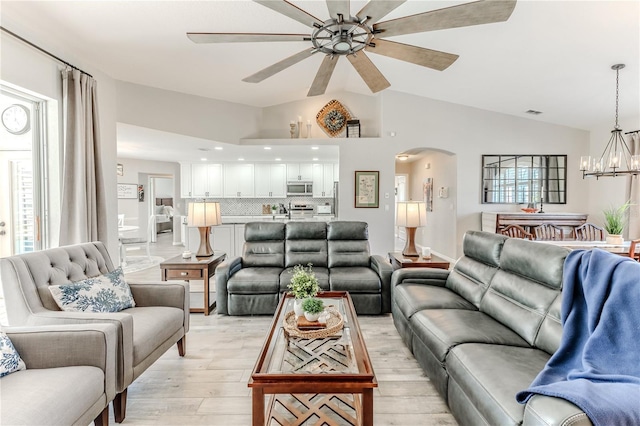 living room featuring ceiling fan with notable chandelier, light wood-type flooring, and lofted ceiling