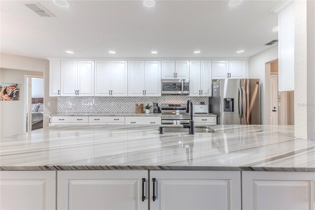 kitchen with kitchen peninsula, sink, appliances with stainless steel finishes, light stone counters, and white cabinetry