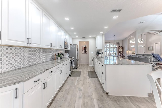 kitchen with stainless steel appliances, ceiling fan, light hardwood / wood-style floors, white cabinetry, and hanging light fixtures