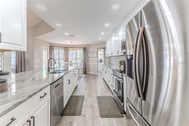 kitchen featuring white cabinetry, sink, pendant lighting, light hardwood / wood-style floors, and appliances with stainless steel finishes