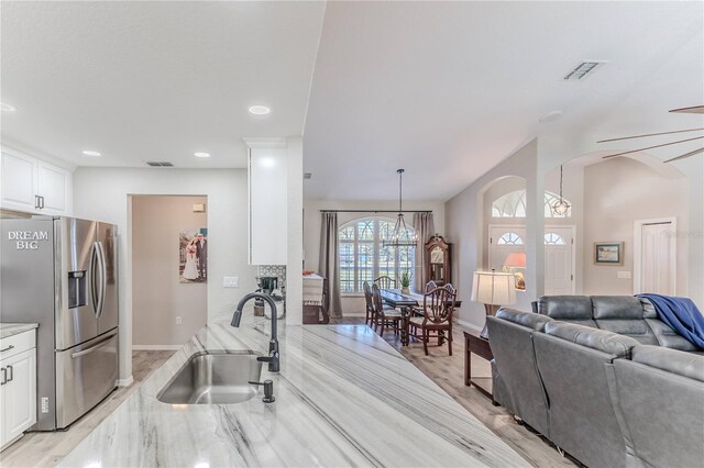 kitchen featuring white cabinets, sink, stainless steel refrigerator with ice dispenser, and hanging light fixtures