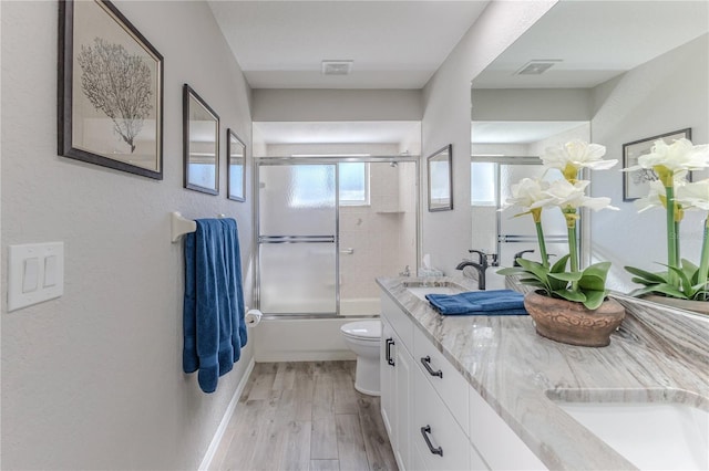 full bathroom with enclosed tub / shower combo, toilet, wood-type flooring, and vanity