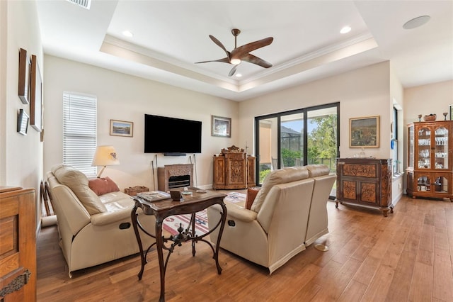 living room with ceiling fan, a raised ceiling, light wood-type flooring, and ornamental molding