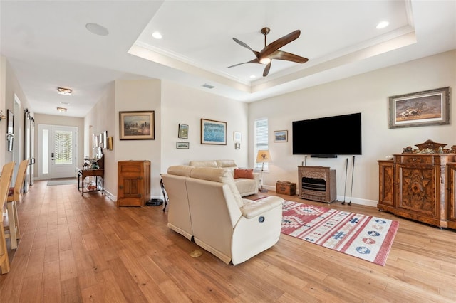 living room with light hardwood / wood-style floors, ornamental molding, ceiling fan, a raised ceiling, and a fireplace