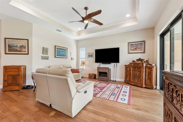 living room featuring ornamental molding, ceiling fan, a tray ceiling, and light hardwood / wood-style floors