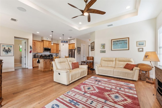 living room with ornamental molding, light wood-type flooring, ceiling fan, and a raised ceiling