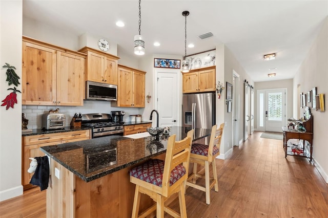 kitchen featuring stainless steel appliances, sink, a kitchen island with sink, pendant lighting, and light wood-type flooring