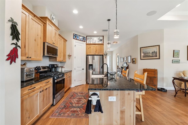 kitchen with a kitchen island with sink, a kitchen breakfast bar, light wood-type flooring, appliances with stainless steel finishes, and decorative light fixtures