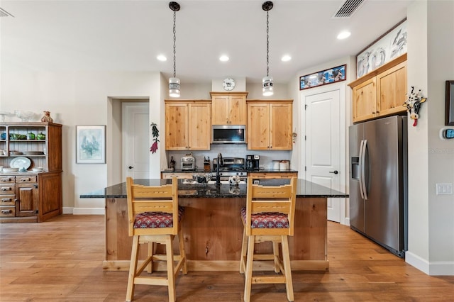 kitchen with stainless steel appliances, dark stone counters, a center island with sink, and light hardwood / wood-style flooring