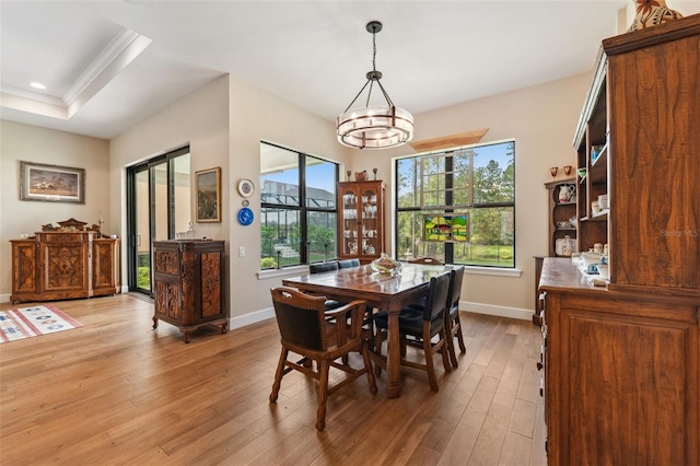 dining area with light hardwood / wood-style floors, a notable chandelier, crown molding, and a tray ceiling