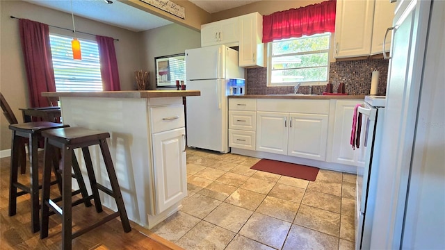 kitchen featuring backsplash, white refrigerator, stove, hanging light fixtures, and white cabinets