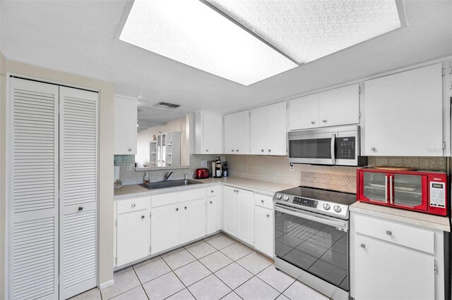 kitchen featuring tasteful backsplash, stainless steel appliances, sink, white cabinetry, and light tile patterned flooring