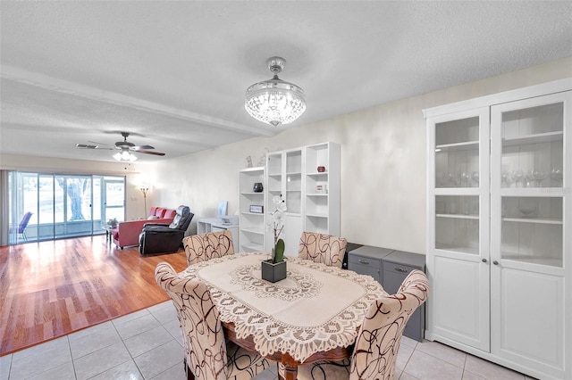 dining space with ceiling fan with notable chandelier, light hardwood / wood-style floors, and a textured ceiling