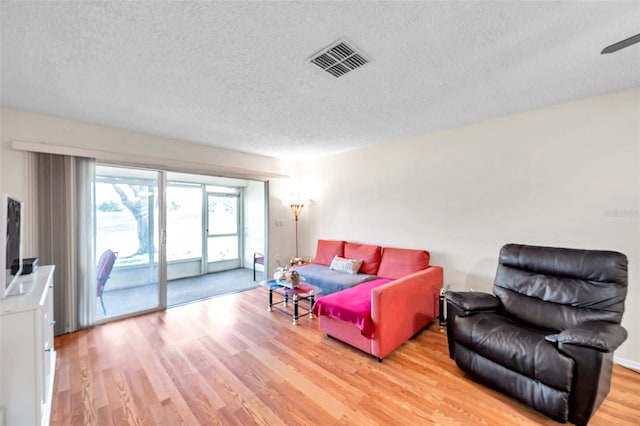 living room with ceiling fan, light wood-type flooring, and a textured ceiling