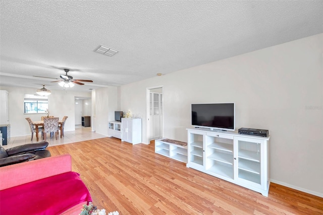 living room with a textured ceiling, light hardwood / wood-style floors, and ceiling fan