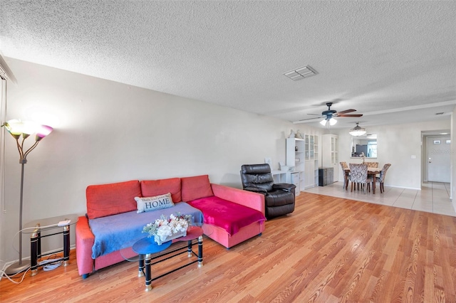 living room with ceiling fan, light wood-type flooring, and a textured ceiling