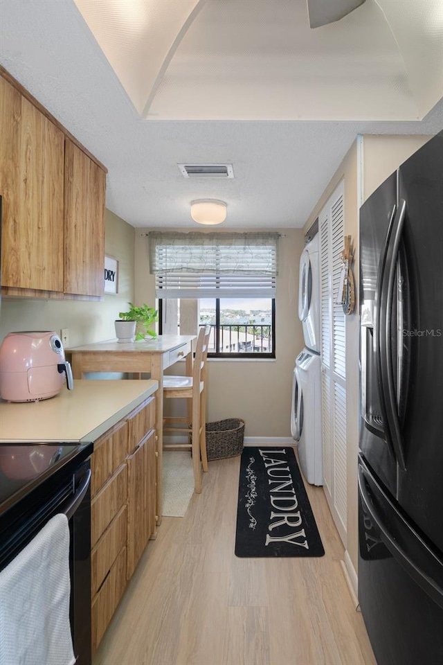 kitchen featuring stacked washer and dryer, black appliances, and light wood-type flooring