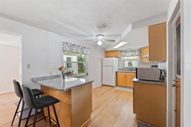 kitchen featuring a breakfast bar, white fridge, kitchen peninsula, ceiling fan, and light wood-type flooring