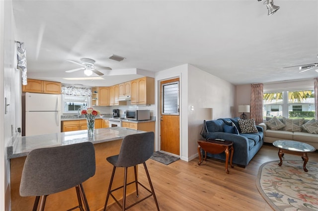 kitchen with a kitchen bar, light brown cabinetry, light wood-type flooring, white appliances, and ceiling fan