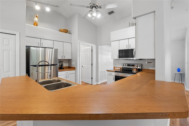 kitchen featuring appliances with stainless steel finishes, high vaulted ceiling, white cabinetry, sink, and kitchen peninsula