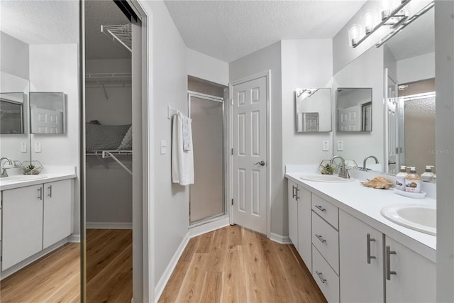 bathroom with a shower with door, wood-type flooring, vanity, and a textured ceiling