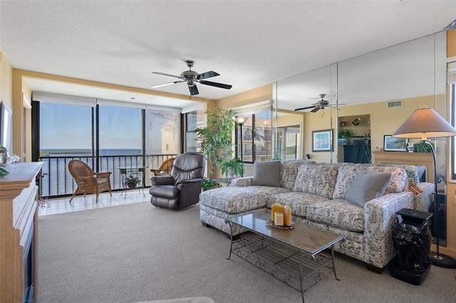 living room with a water view, light carpet, ceiling fan, and a textured ceiling