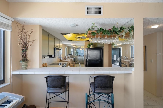 4620 Bay Blvd Unit 1148, Port Richey, FL 34668 - kitchen featuring freestanding refrigerator, stainless steel microwave, tile countertops, light tile patterned flooring, and a peninsula