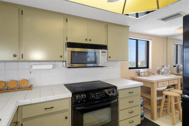 4620 Bay Blvd Unit 1148, Port Richey, FL 34668 - kitchen featuring stainless steel microwave, black range with electric cooktop, tile countertops, decorative backsplash, and a textured ceiling