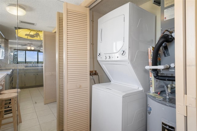 laundry room with electric water heater, light tile patterned flooring, stacked washing maching and dryer, and a textured ceiling