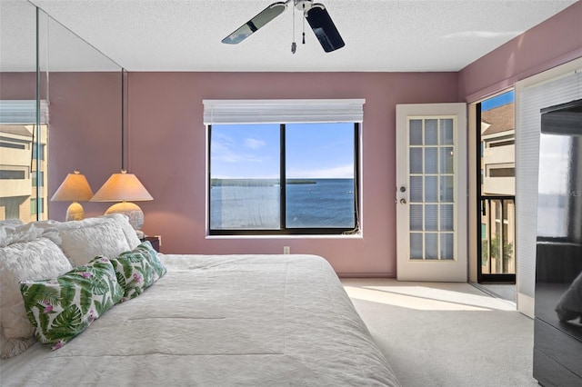 bedroom featuring a textured ceiling, carpet floors, a water view, and ceiling fan