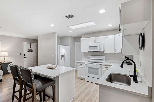 kitchen featuring a kitchen breakfast bar, white appliances, sink, light hardwood / wood-style flooring, and white cabinetry