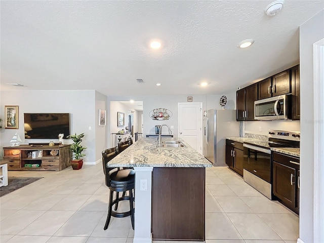 kitchen with sink, stainless steel appliances, a kitchen bar, a kitchen island with sink, and light tile patterned floors