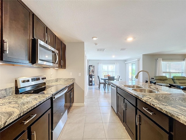 kitchen with sink, light tile patterned floors, a textured ceiling, stone countertops, and stainless steel appliances