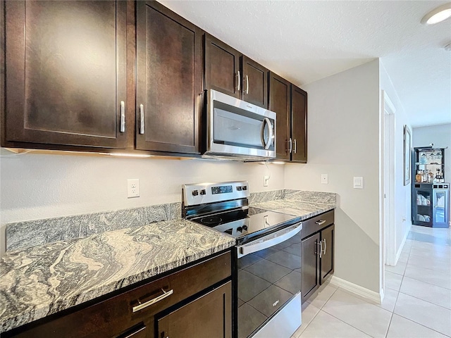 kitchen featuring light tile patterned floors, light stone counters, dark brown cabinetry, and appliances with stainless steel finishes