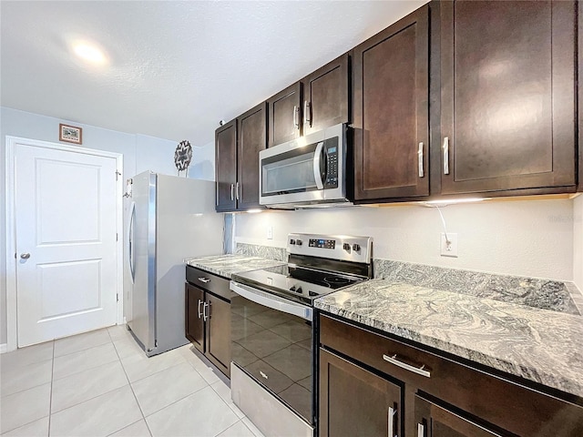 kitchen with light tile patterned floors, a textured ceiling, appliances with stainless steel finishes, light stone counters, and dark brown cabinetry