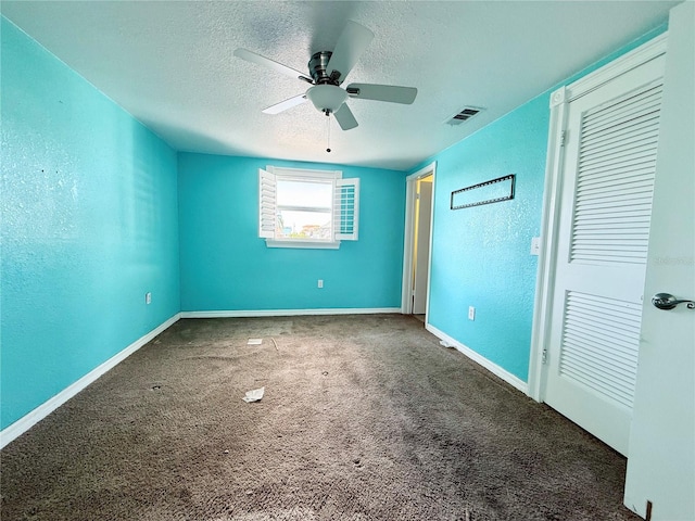 unfurnished bedroom featuring ceiling fan, dark carpet, and a textured ceiling