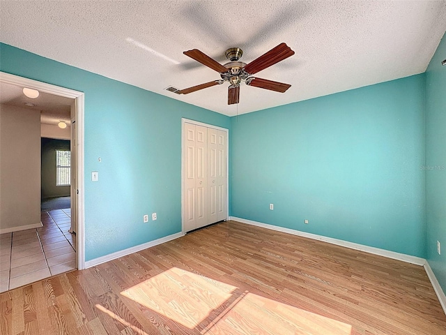 unfurnished bedroom featuring a textured ceiling, light wood-type flooring, a closet, and ceiling fan