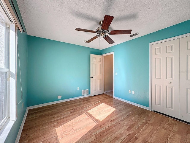 unfurnished bedroom featuring ceiling fan, light wood-type flooring, a textured ceiling, and a closet