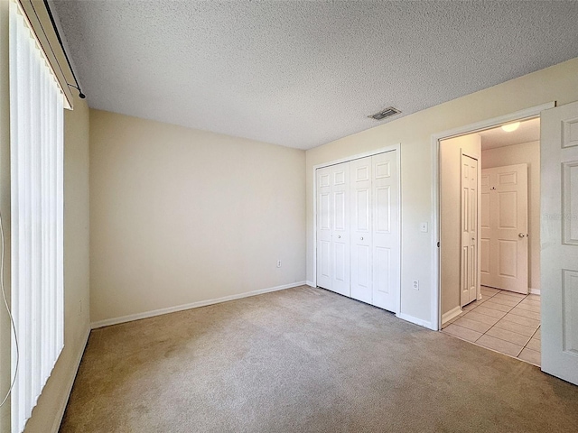 unfurnished bedroom featuring light colored carpet, a textured ceiling, and a closet