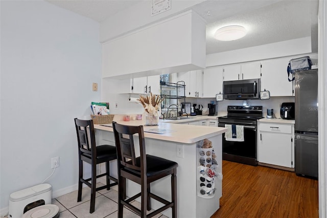 kitchen with dark wood-type flooring, white cabinets, a kitchen breakfast bar, sink, and stainless steel appliances