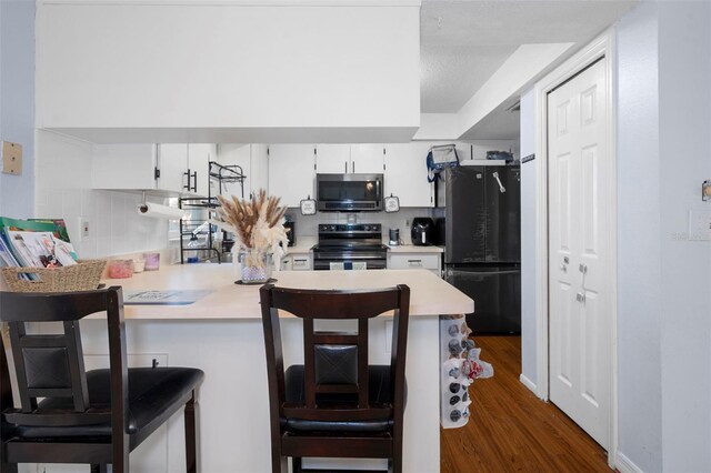 kitchen with black / electric stove, white cabinets, dark hardwood / wood-style floors, fridge, and a kitchen bar