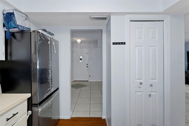 kitchen with stainless steel fridge, a textured ceiling, white cabinetry, and light tile patterned flooring