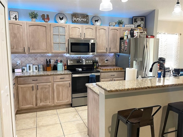 kitchen with light stone counters, a kitchen bar, stainless steel appliances, and hanging light fixtures